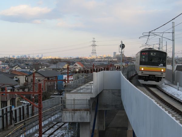 南多摩駅に進入する南武線205系。遠方には新宿副都心・東京スカイツリー。